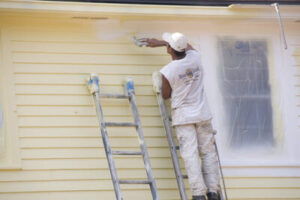 Man applying yellow Rhino Shield coating to side of house